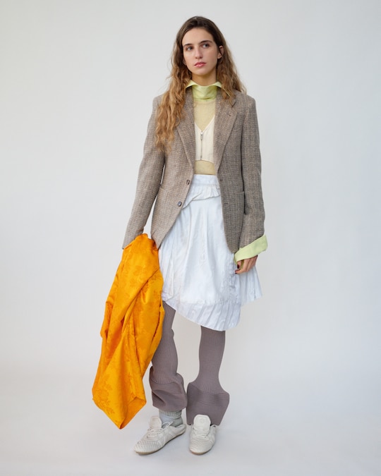 Giacca in cashmere e mohair, LORO PIANA.Borsa Balloon 2 in nylon, indossata come gilet, top in maglia di cotone (660 €), camicia (350 €) e pantaloni in mix di poliestere riciclato (580 €), tutto ISSEY MIYAKE.Gonna in seta, MARTINE ROSE (750 €). Sneakers in pelle, LOUIS VUITTON (735 €). Mantello in seta jacquard, COLLEEN ALLEN (2.890 $).