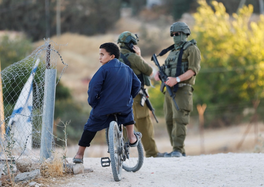 Un ragazzino palestinese è seduto su una bicicletta davanti a soldati dell’esercito israeliano durante una manifestazione per commemorare il primo anniversario della morte dell’attivista palestinese Odeh Hathaleen, a Umm al-Khair, nella Cisgiordania occupata da Israele, il 28 luglio 2026. REUTERS/Mussa Qawasma (REUTERS)