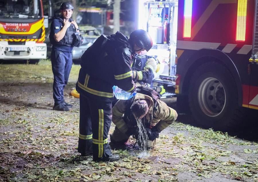 Un soccorritore versa dell’acqua su un collega mentre lavorano sul luogo di un condominio colpito da un missile russo a Kiev (REUTERS)