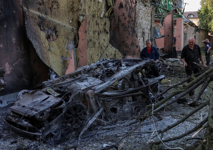 Alcuni residenti osservano un’auto bruciata nel luogo colpito da un missile russo a Kiev (REUTERS)