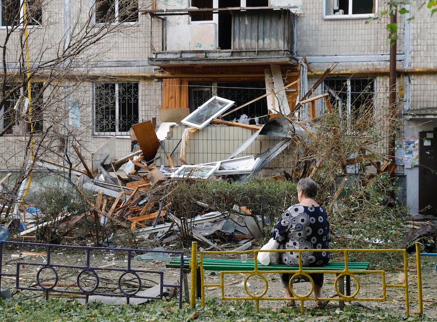 Una donna del posto siede davanti al luogo colpito da un missile russo contro un edificio residenziale a Kiev (EPA)