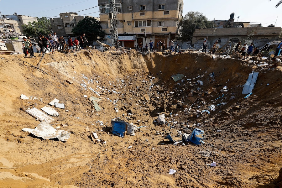 Alcuni palestinesi si trovano accanto a un cratere dopo un attacco israeliano contro un deposito di medicinali – secondo quanto riferito dal personale sanitario – a Deir al-Balah, nella Striscia di Gaza centrale (REUTERS)