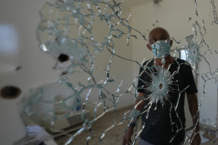Un abitante si trova dietro uno specchio crivellato di fori di proiettile all'interno della propria abitazione, in seguito a un'operazione militare israeliana a Zawtar al-Gharbieh, in Libano. (Foto AP/Hassan Ammar/APN)