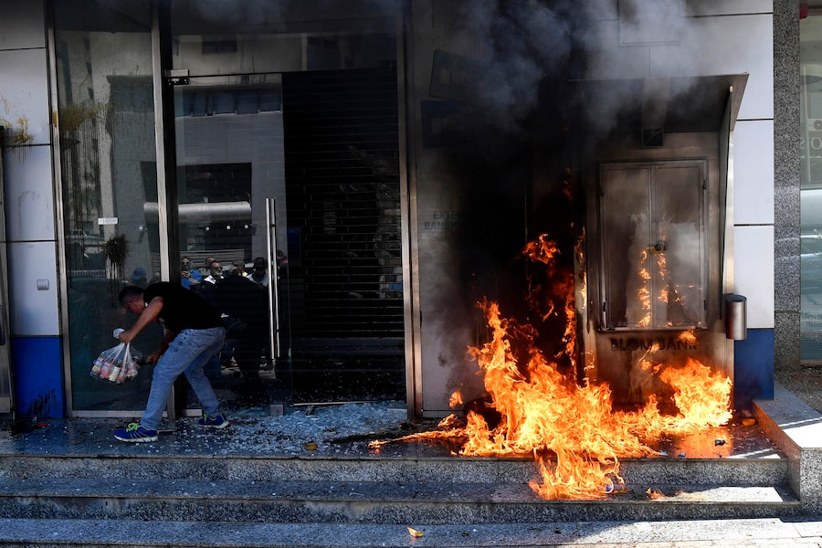 Un uomo è in piedi vicino a un falò acceso davanti a una banca durante una manifestazione dei correntisti libanesi che non riescono ancora a prelevare i propri risparmi in valuta estera a Beirut, in Libano. I clienti delle banche, in gran parte impossibilitati ad accedere ai propri conti in valuta estera a seguito della crisi finanziaria del 2019, si sono radunati in Piazza dei Martiri prima di marciare verso il sobborgo di Sin el-Fil, a est di Beirut, dove diverse facciate di banche sono state vandalizzate. (EPA/Abbas Salman)