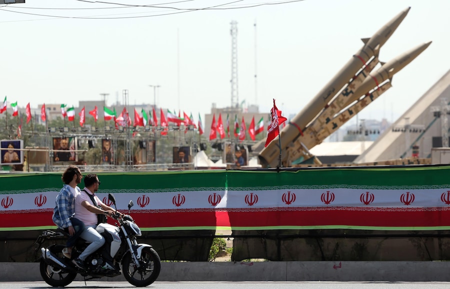 Alcuni motociclisti passano davanti ai missili iraniani “Zolfaghar” esposti sopra uno striscione raffigurante il presidente degli Stati Uniti Trump in piazza Azadi a Teheran, in Iran. (EPA/Abedin Taherkenareh)