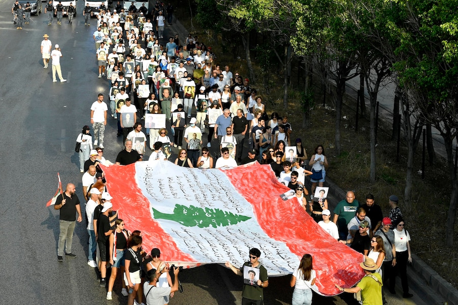 Alcune persone sventolano la bandiera libanese durante una marcia in memoria delle vittime dell’esplosione del porto di Beirut del 2020, a Beirut. Il Libano commemora i sei anni dall’esplosione che il 4 agosto 2020 ha devastato l’area portuale di Beirut, causando la morte di almeno 200 persone e il ferimento di altre migliaia. Si ritiene che l’esplosione sia stata causata dall’accensione di circa 2.750 tonnellate di nitrato di ammonio stoccate in un magazzino del porto. (EPA/Abbas Salman)