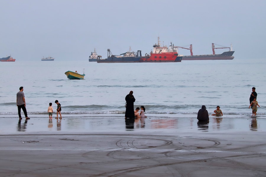 Mercoledì 5 agosto 2026, alcune persone trascorrono del tempo in spiaggia mentre navi mercantili sono ancorate nello Stretto di Ormuz, al largo di Bandar Abbas, in Iran. (Amirhosein Khorgooi/ISNA via AP) (APN)