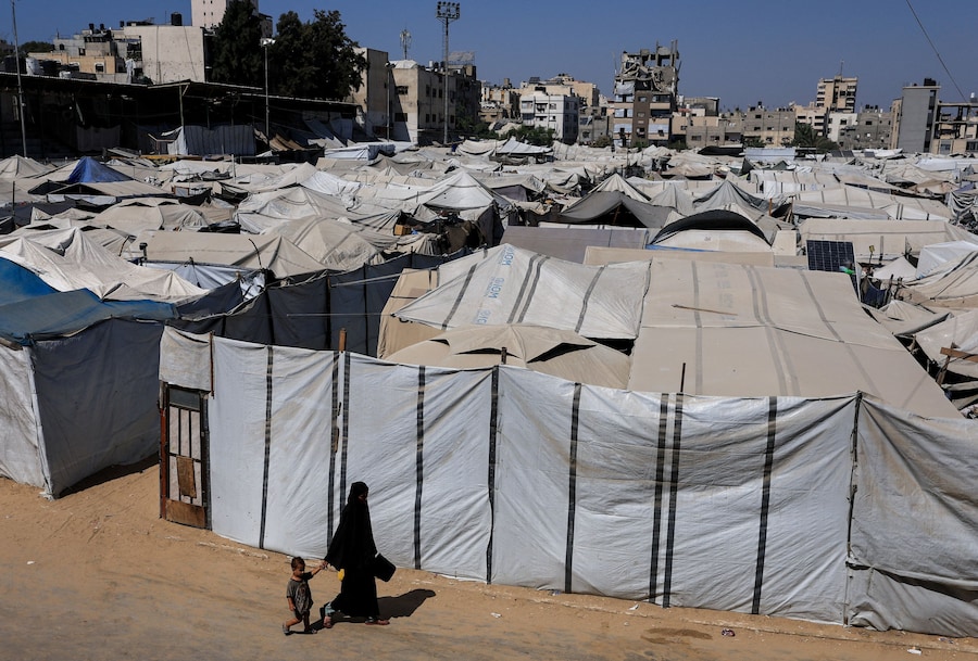 Una donna palestinese e un bambino camminano accanto a un accampamento di tende che ospita palestinesi sfollati a Gaza City (REUTERS)