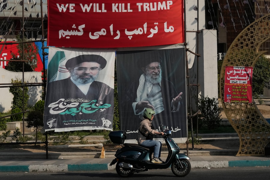 Una moto passa davanti a uno striscione su cui si legge, in inglese e in farsi, "Uccideremo Trump", e striscioni con i ritratti del defunto leader supremo iraniano, l’ayatollah Ali Khamenei, a destra, e di suo figlio, l’ayatollah Mojtaba Khamenei, suo successore, in una piazza di Teheran, in Iran (APN)