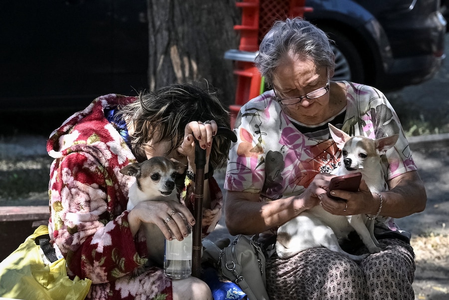 Alcuni residenti, accompagnati dai propri cani, sono seduti nei pressi di un complesso residenziale colpito da un attacco aereo russo a Zaporizhzhia, Ucraina (REUTERS)
