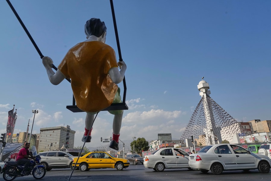 Alcuni veicoli passano davanti alla statua di un ragazzino sull’altalena in una piazza di Teheran, in Iran (APN)