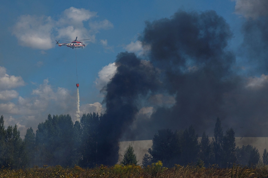 Un elicottero antincendio scarica acqua su un magazzino alimentare danneggiato durante gli attacchi con droni russi nella regione di Kiev (REUTERS)