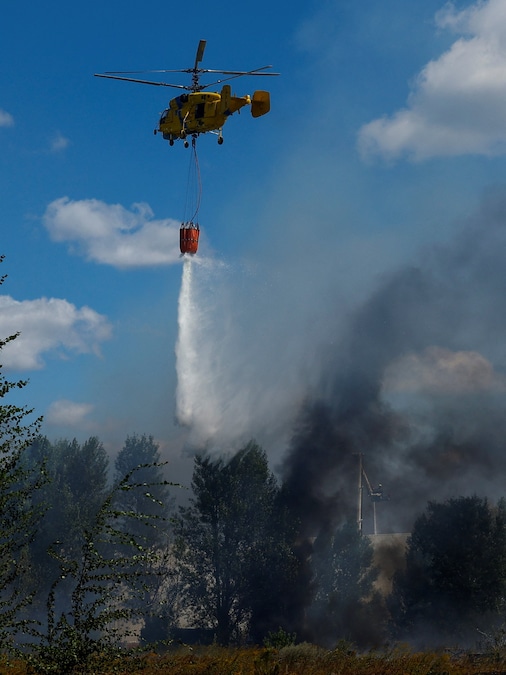Un elicottero antincendio scarica acqua su un magazzino alimentare danneggiato durante gli attacchi con droni russi nella regione di Kiev (REUTERS)