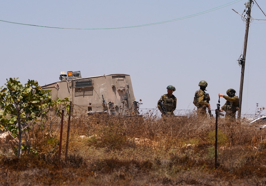 Soldati dell’esercito israeliano in piedi vicino a un’abitazione palestinese assediata dai coloni israeliani nel villaggio di Qusra, in Cisgiordania occupata da Israele, il 13 agosto 2026. REUTERS/Ali Sawafta (REUTERS)
