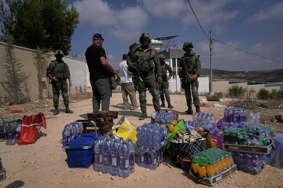 Venerdì 14 agosto 2026, nel villaggio di Qusra, nella Cisgiordania occupata, a sud di Nablus, alcuni attivisti accumulano scorte di cibo e acqua davanti ai soldati dell’esercito israeliano che stanno bloccando la strada che conduce alle abitazioni di tre famiglie palestinesi assediate dai coloni israeliani da sei giorni. (Foto AP/Majdi Mohammed) (APN)