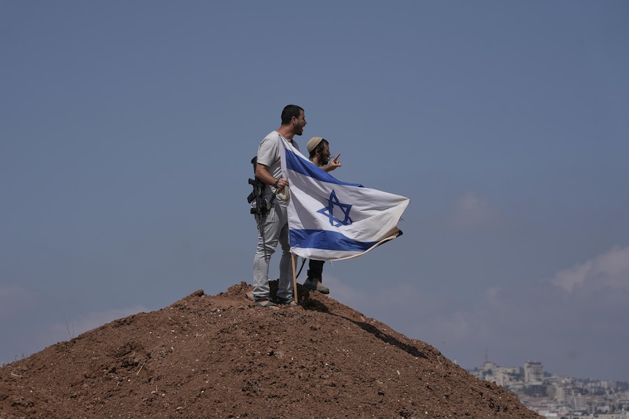 Coloni israeliani issano una bandiera israeliana sulla cima di una collina dopo che era stata rimossa da attivisti per la pace israeliani e stranieri durante una manifestazione a sostegno dei proprietari terrieri locali, le cui proprietà rischiano di essere confiscate dai coloni, alla periferia della città di Beit Sahour, in Cisgiordania, venerdì 14 agosto 2026. (APS)