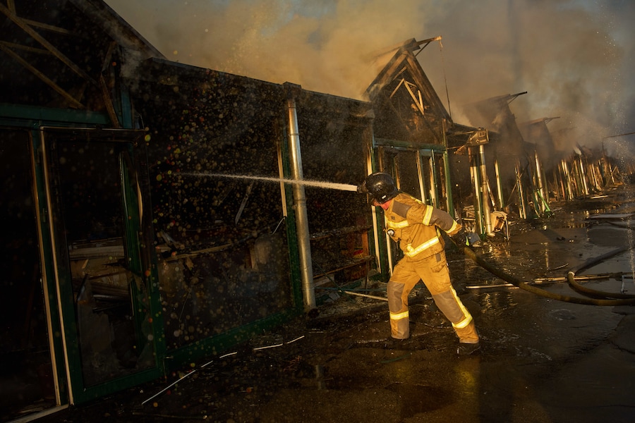 I vigili del fuoco cercano di spegnere un incendio divampato in un mercatino dei libri della città a seguito di un attacco missilistico russo a Kiev, in Ucraina. (APN)