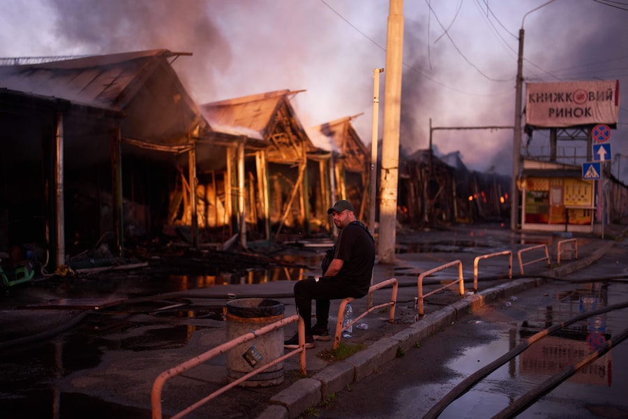 Un libraio è seduto mentre i vigili del fuoco cercano di spegnere un incendio divampato in un mercato librario della città a seguito di un attacco missilistico russo a Kiev, in Ucraina. (APN)