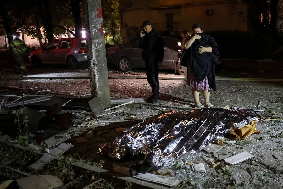 Alcune persone sono in piedi accanto al corpo di un residente ucciso sul luogo di un condominio colpito da un missile russo, nel contesto dell'attacco della Russia all'Ucraina, a Kiev. (REUTERS)
