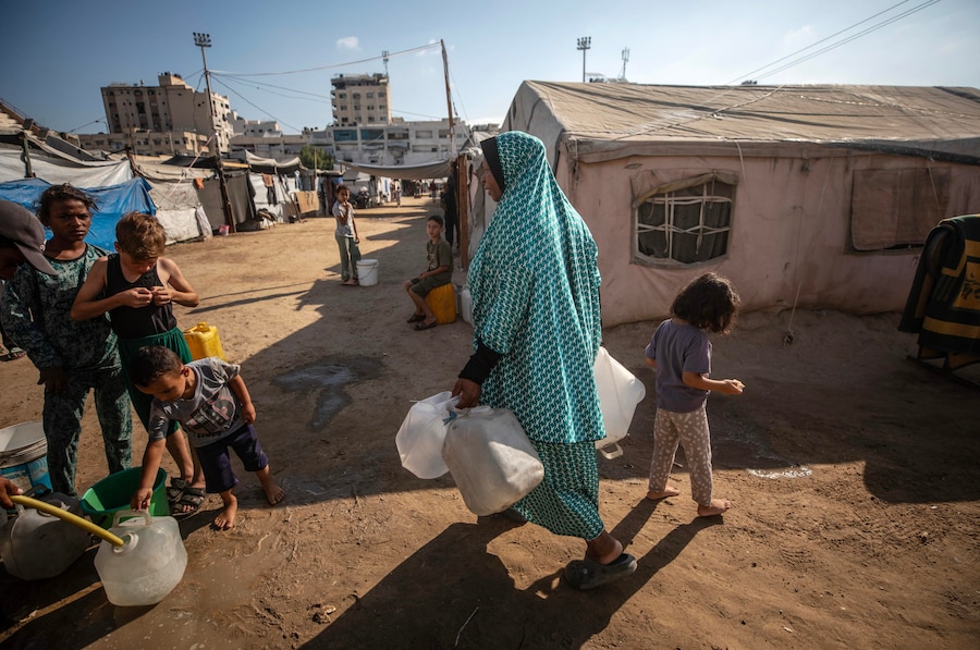 I palestinesi sfollati fanno la fila per ritirare l’acqua potabile in un campo profughi nel centro di Gaza City (EPA)