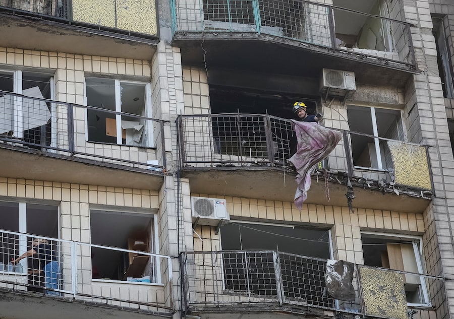 Un soccorritore rimuove le macerie da un balcone di un condominio danneggiato durante l’attacco missilistico a Kiev, Ucraina (REUTERS)