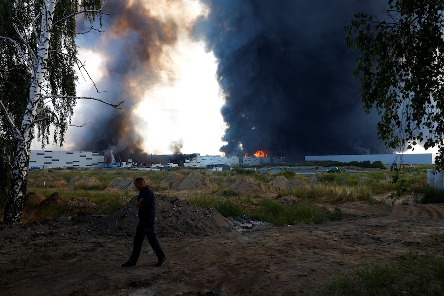 Una persona passa mentre il fumo si alza sopra un magazzino, colpito da un attacco con droni russi, nel contesto dell'offensiva russa contro l'Ucraina, nella regione di Kiev. (REUTERS/Valentyn Ogirenko)