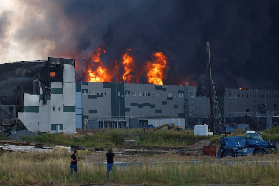 Alcuni uomini osservano il fumo che si alza da un magazzino in fiamme, colpito da un attacco con droni russi nel corso dell'offensiva russa contro l'Ucraina, nella regione di Kiev. (REUTERS/Valentyn Ogirenko)