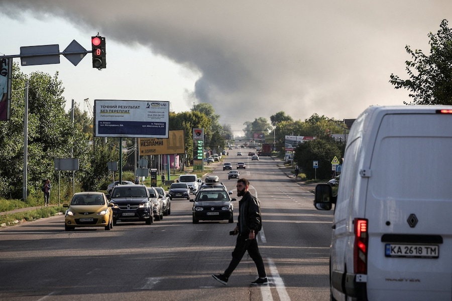 Un uomo attraversa una strada mentre sullo sfondo si alza il fumo a seguito di un attacco sferrato durante la notte da un drone russo, nel contesto dell'offensiva russa contro l'Ucraina, nella regione di Kiev, Ucraina, il 28 agosto 2026. (REUTERS/Alina Smutko)