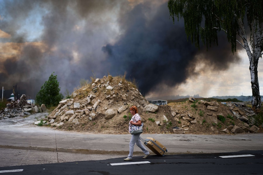 Una donna cammina lungo una strada mentre il fumo sale da un magazzino distrutto in seguito a un attacco con droni russi alla periferia di Kiev. (Foto AP/Francisco Seco/APN)