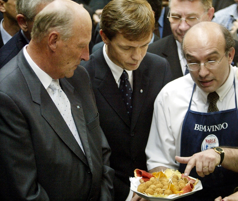 Un venditore di prodotti ittici brasiliano non identificato (a destra) mostra degli involtini di merluzzo essiccato fritto al re Harald V di Norvegia (a sinistra) e al viceconsole norvegese in Brasile, Per Christian Enge (al centro), durante una visita al Mercato Municipale di San Paolo, in Brasile. Brazil REUTERS/Paulo Whitaker/File Photo (REUTERS)