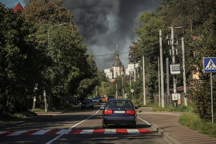 Un'auto attraversa una zona residenziale mentre sullo sfondo si alza il fumo a seguito di un attacco con droni russi, nella regione di Kiev, Ucraina, il 29 agosto 2026. (REUTERS/Alina Smutko)