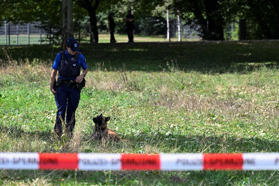 Un agente di polizia è in piedi con il cane accanto al nastro di delimitazione, nei pressi del luogo in cui, secondo la polizia, si è verificata una sparatoria mortale durante un rave a Schachen, nei pressi di Aarau, in Svizzera, il 30 agosto 2026. (REUTERS/Romina Amato)