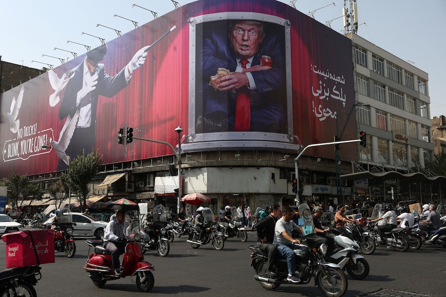 Alcune persone passano in auto vicino a un cartellone pubblicitario raffigurante il presidente degli Stati Uniti Donald Trump su un edificio a Teheran. (via REUTERS)