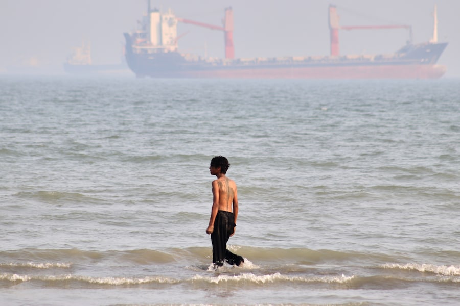 Un ragazzo cammina nell'acqua bassa mentre alcune navi mercantili sono ancorate nello Stretto di Ormuz al largo di Bandar Abbas, in Iran. (APN)