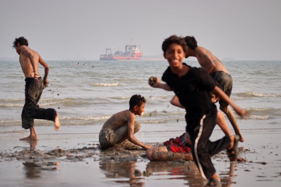 Dei bambini giocano su una spiaggia mentre alcune navi mercantili sono ancorate nello Stretto di Ormuz al largo di Bandar Abbas, in Iran. (APN)