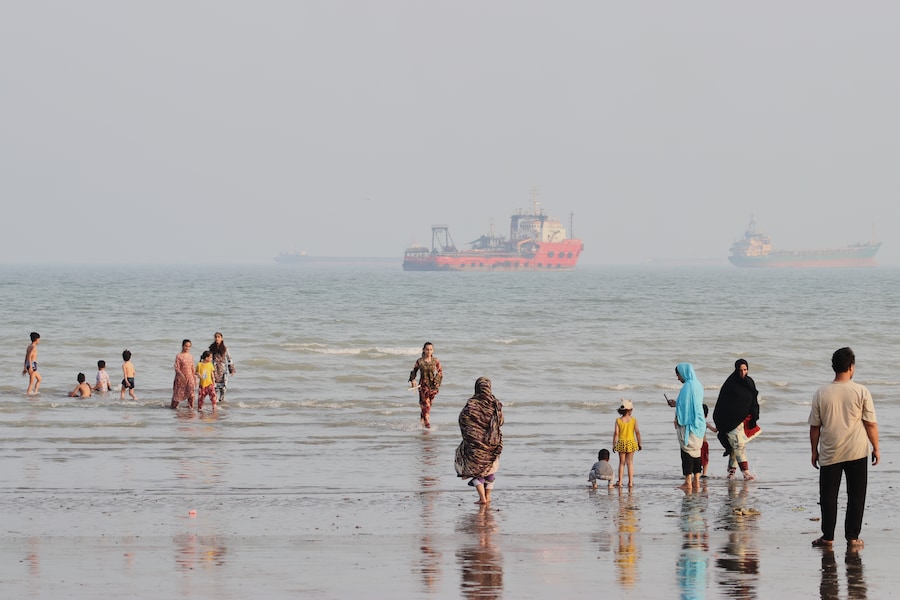 La gente trascorre il tempo in spiaggia mentre alcune navi mercantili sono ancorate nello Stretto di Hormuz al largo di Bandar Abbas, in Iran. (APN)