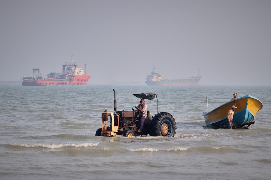 Un trattore trascina una barca fuori dal mare mentre alcune navi mercantili sono ancorate nello Stretto di Hormuz al largo di Bandar Abbas, in Iran. (APN)
