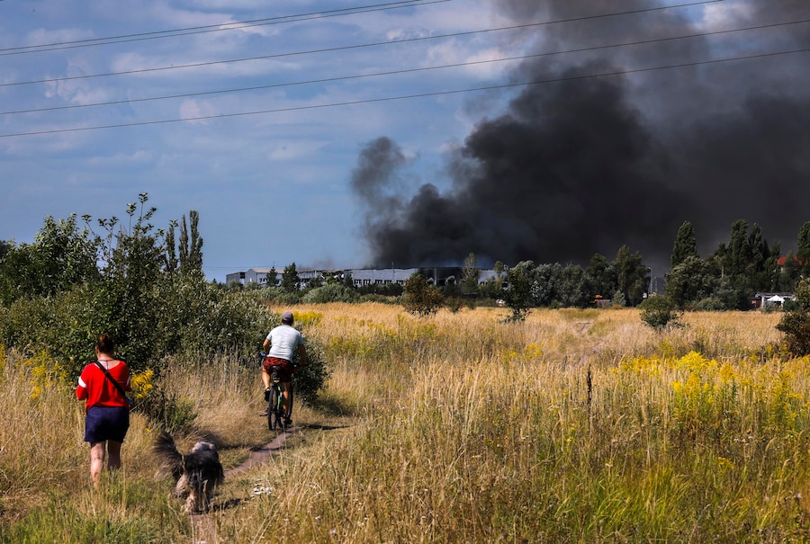 Alcune persone camminano su un campo mentre il fumo si alza sul luogo di un attacco russo nei pressi di Kiev. (EPA)