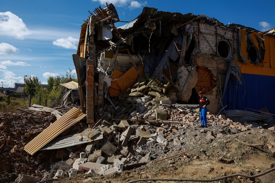 Un adolescente è in piedi accanto a un cratere formatosi vicino all’edificio di un supermercato in seguito all’impatto di un missile russo, nel corso dell’attacco russo all’Ucraina. (REUTERS)