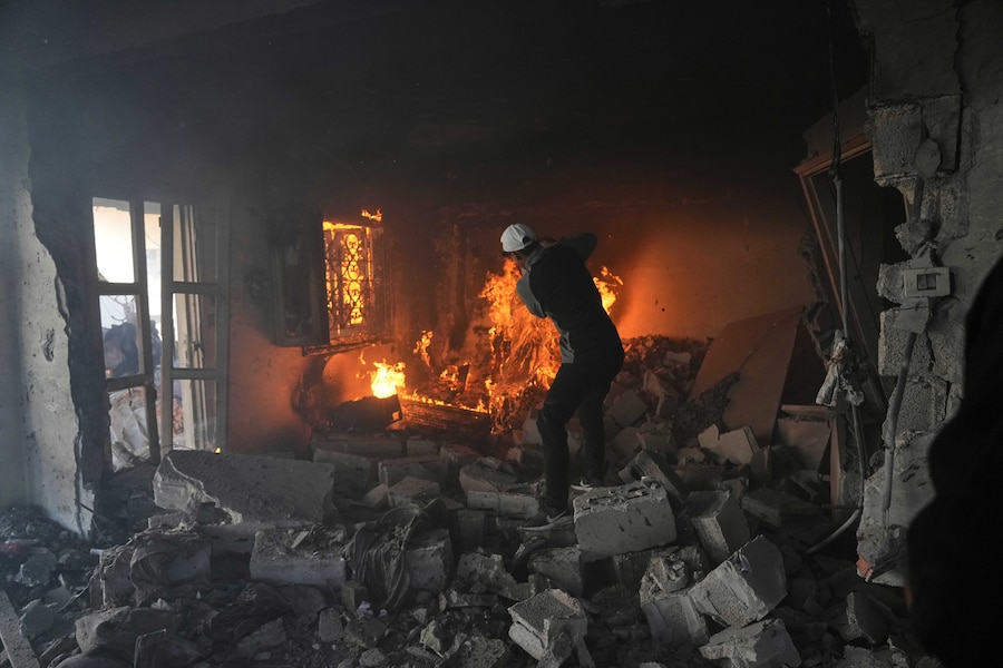 Un uomo palestinese cerca di spegnere un incendio tra le macerie di un edificio in seguito a un attacco aereo israeliano nella città di Gaza (APN)