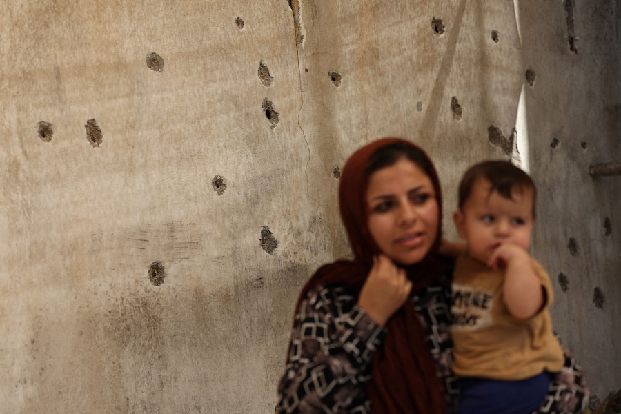 Una donna è in piedi con un bambino vicino ai segni lasciati dalle schegge sul muro di un'abitazione dopo un attacco avvenuto il 28 febbraio, a Lamerd, in Iran, il 12 settembre 2026. Majid Asgaripour/WANA (West Asia News Agency) via REUTERS (via REUTERS)