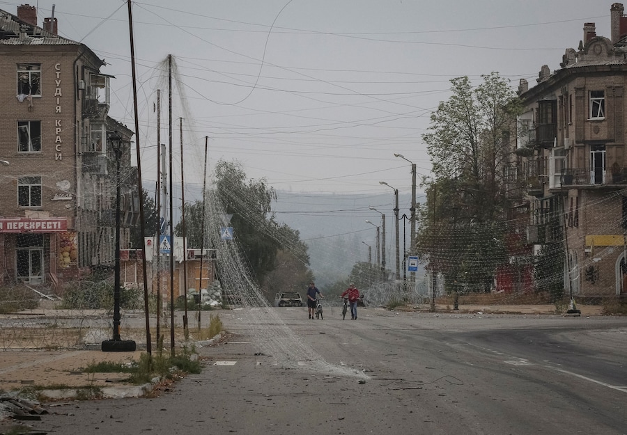 I residenti spingono le biciclette lungo una strada ricoperta da reti anti-drone e con filo spinato installato nelle vicinanze, mentre la Russia attacca l’Ucraina, nella città di Druzhkivka, in prima linea nella regione di Donetsk. (REUTERS)