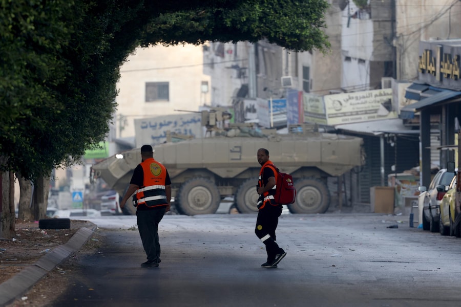 Operatori sanitari palestinesi camminano mentre mezzi corazzati israeliani bloccano l’ingresso del campo profughi di Al-Ain durante un’operazione militare a ovest della città di Nablus, in Cisgiordania, il 17 settembre 2026. Le forze israeliane hanno fatto irruzione nel campo di Al-Ain, a ovest di Nablus, all’alba del 17 settembre. (EPA)