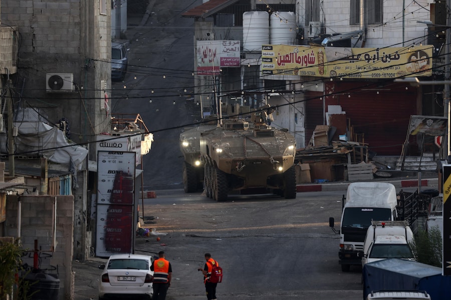 Operatori sanitari palestinesi camminano mentre mezzi corazzati israeliani bloccano l’ingresso del campo profughi di Al-Ain durante un’operazione militare a ovest della città di Nablus, in Cisgiordania, il 17 settembre 2026. Le forze israeliane hanno fatto irruzione nel campo di Al-Ain, a ovest di Nablus, all’alba del 17 settembre. (EPA)