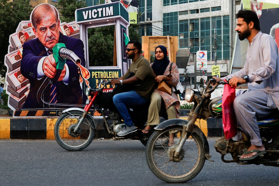 Alcuni motociclisti passano davanti a un ritratto del primo ministro pakistano Shehbaz Sharif, esposto in segno di protesta contro l’aumento dei prezzi del carburante nel contesto del conflitto tra Stati Uniti e Iran, in vista dell’introduzione a livello nazionale di un programma governativo che offre un sussidio di 100 rupie al litro alle motociclette, risciò e veicoli fino a 800 cc, a Karachi, in Pakistan. (REUTERS/Akhtar Soomro)