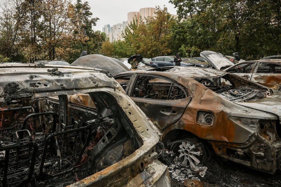 Alcuni residenti si trovano vicino a veicoli carbonizzati sul luogo di un attacco missilistico russo nei pressi di un centro di assistenza sanitaria di base, nel contesto dell'attacco della Russia all'Ucraina a Kiev. (REUTERS)