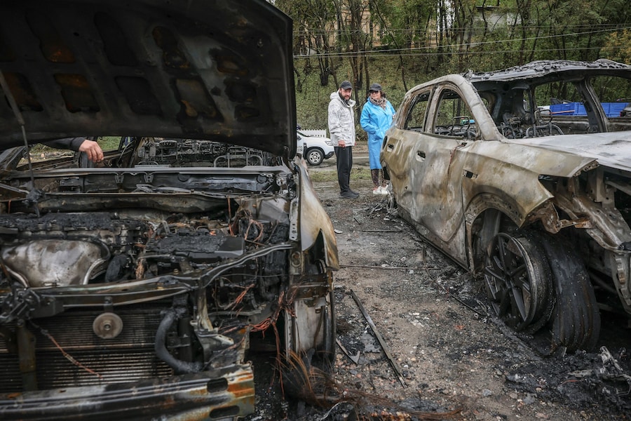 Alcuni residenti si trovano vicino a veicoli carbonizzati sul luogo di un attacco missilistico russo nei pressi di un centro di assistenza sanitaria di base, nel contesto dell'offensiva russa contro l'Ucraina a Kiev. (REUTERS)