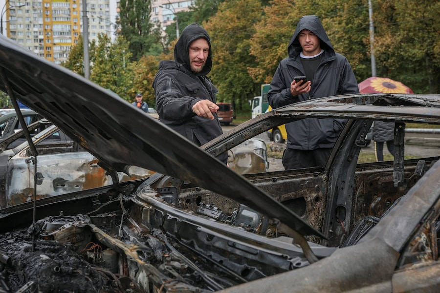 Alcuni uomini osservano un'auto bruciata sul luogo di un attacco missilistico russo nei pressi di un centro di assistenza sanitaria di base, nel contesto dell'attacco della Russia all'Ucraina a Kiev. (REUTERS)
