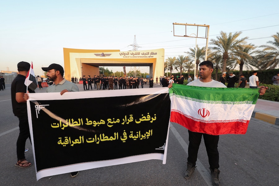 I manifestanti espongono uno striscione e una bandiera iraniana durante una manifestazione contro le restrizioni statunitensi che colpiscono le attività aeronautiche iraniane e il loro impatto sui voli tra l’Iran e l’Iraq, all’esterno dell’aeroporto internazionale di Najaf, a Najaf, in Iraq. (REUTERS)