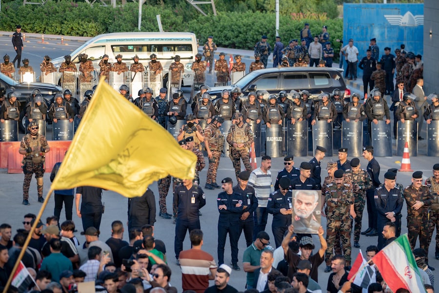 Le forze di sicurezza irachene montano la guardia mentre un manifestante tiene in mano un ritratto del defunto generale iraniano Qassem Soleimani durante una protesta contro la sospensione dei voli tra Iraq e Iran, davanti all’aeroporto internazionale di Najaf, a Najaf, in Iraq. (APN)